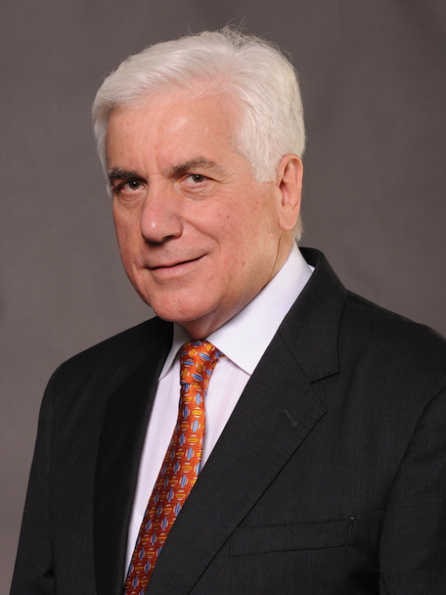 head shot of white short haired male wearing a black suit, light shirt and patterned red tie
