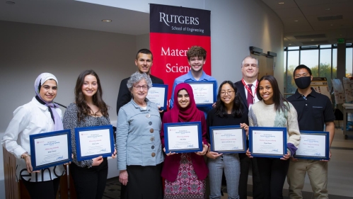 Group of eight students holding plaques with a female professor and a male teaching professor.