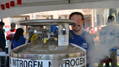 Graduate student wearing pink glasses standing behind nitrogen tank.