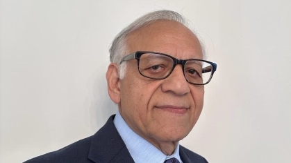 Head shot of male in a dark suit, blue shirt and dark blue tie, wearing glasses and smiling. 