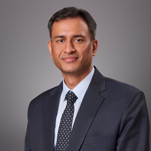 Headshot of male with short black hair wearing a black suit, tie, and w white button down shirt.