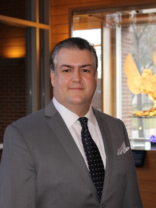 Head shot of male with short hair wearing a grey suit, white shirt, and black tie.