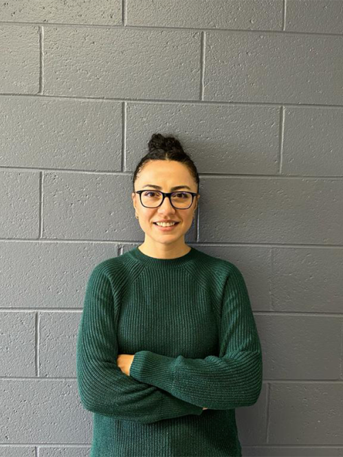 Head shot of woman with her hair up in a bun, folding her arms wearing a green sweater, eyeglasses