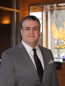 Head shot of male with short hair wearing a grey suit, white shirt, and black tie.