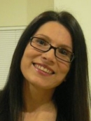 Head shot of smiling female tilting her head to the side with long black hair wearing eyeglasses.