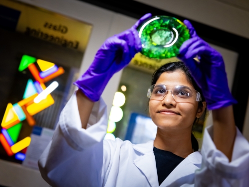 Female student looking at poured green glass in glass laboratory.