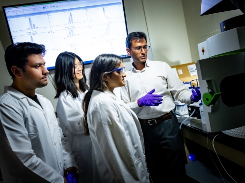 Professor instructing three graduate students in materials lab.