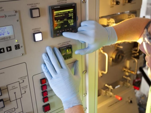 Male student wearing safety glasses and blue protective gloves pushes buttons on a mechanical device.