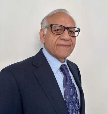 Head shot of male in a dark suit, blue shirt and dark blue tie, wearing glasses and smiling. 