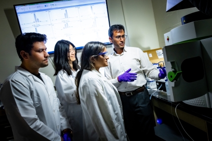 Professor instructing three graduate students in materials lab.