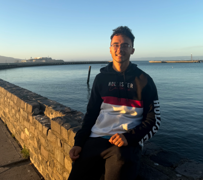 Student poses on a brick wall overlooking a lake.
